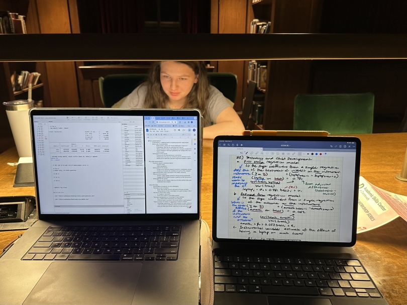 A horizontal photo of two screens with Economics notes and regression tables taken in the Tower Room