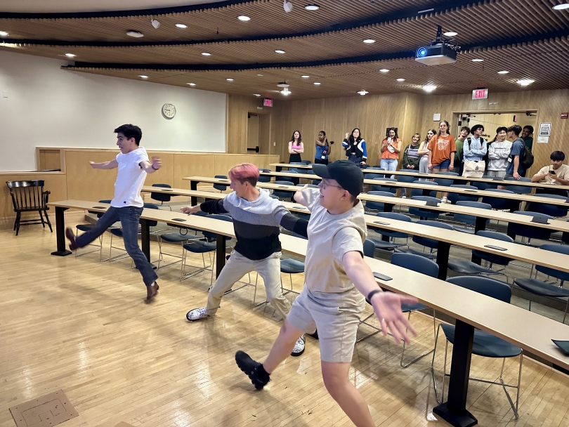 3 students dance at the center of a room following the Just Dance screen on the projector.