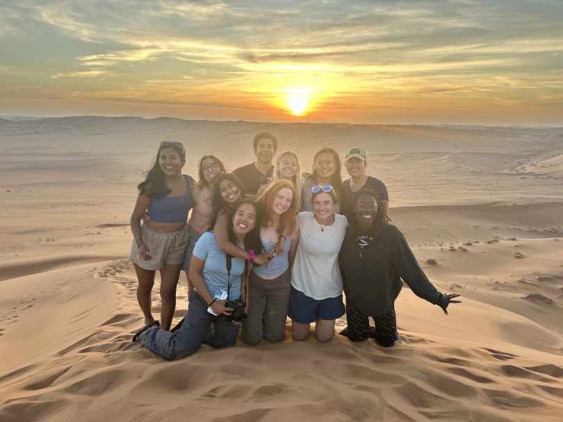 11 FSP participants smile during the sunset on top of a sand dune.