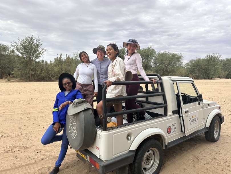 A group of four Dartmouth student and one Gobabeb researcher pose on the back of an open-air vehicle during a cloudy day in the desert.