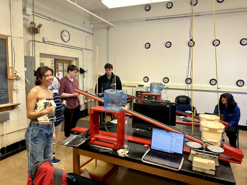 My lab partner smiles with a thumbs-up as we perform a Physics experiment using a red ramp, small ball, and water timer.