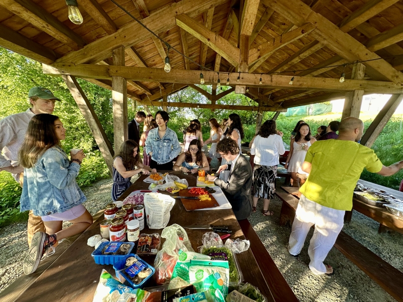 A group of people wearing formal clothing make pizzas from fresh ingredients at the Organic Farm.