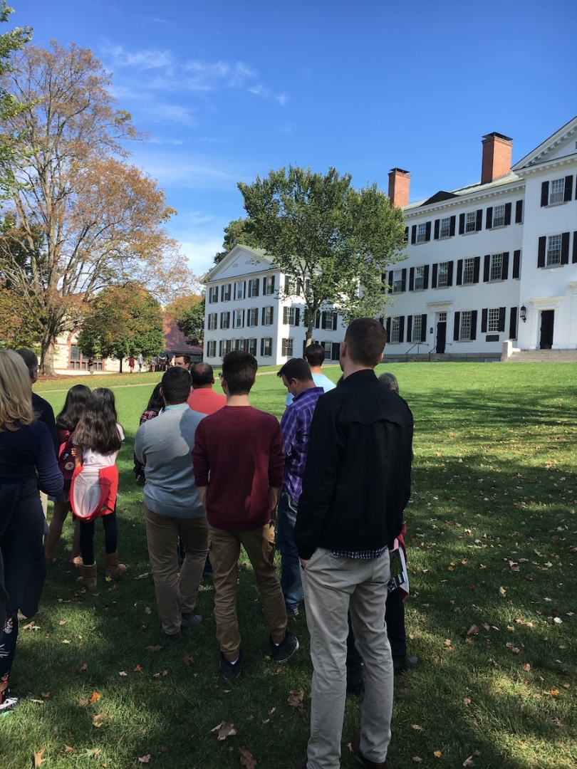 A tour group stands in front of a green-and-white building on a sunny hill.