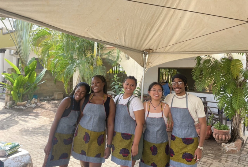 A group of five Dartmouth students on a study abroad program in Ghana, wearing aprons during a cooking class