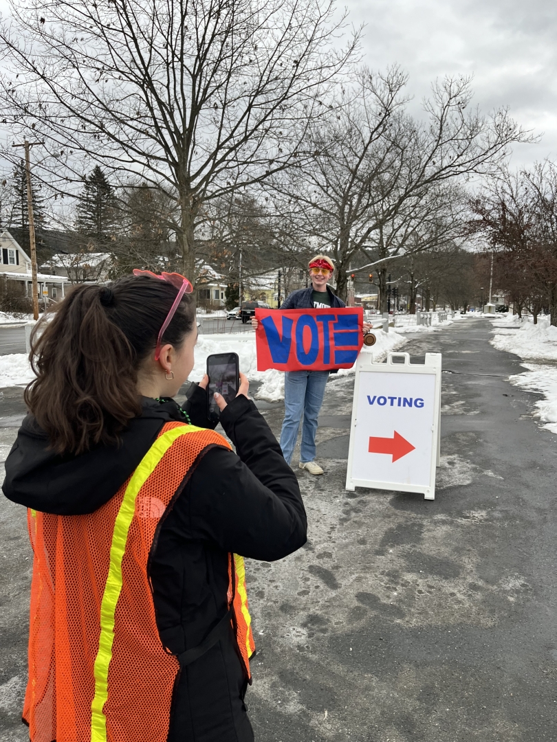 My friend, Bea, takes a photo of fellow Civics member Will holding a "Vote" sign in front of a polling location. Both students are wearing flair!