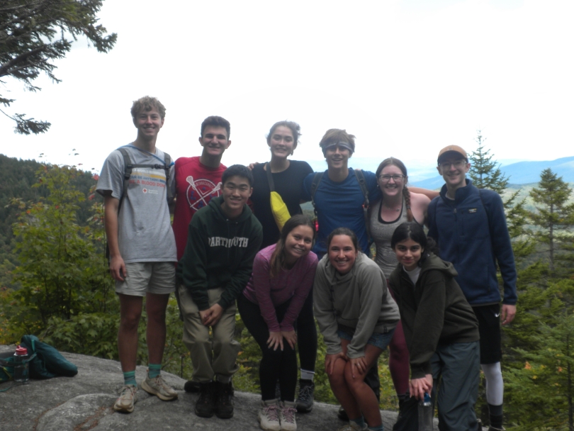 martin and his trip stand shoulder to shoulder and pose with a view of the forest behind them as they hike Mt. Cartigan