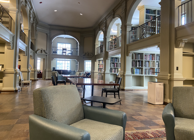 A large two-story library with arched thresholds. The center of the room is an open space, but there are two stories of desks on the walls. The floor is checkered wood, and all the coaches are a light green/teal.