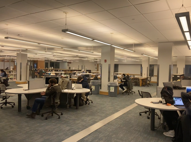 A large open room with carpeted floors and tables scattered around. 