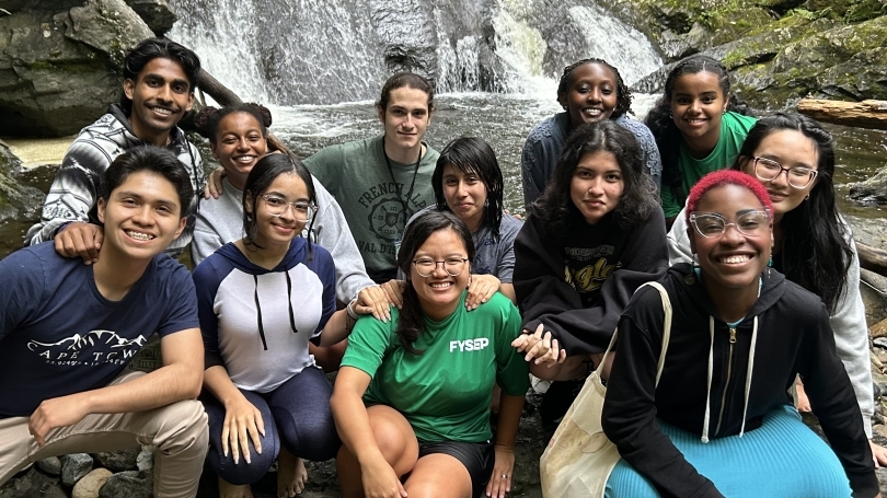 A group of students are beaming in front of a dazzling waterfall. 