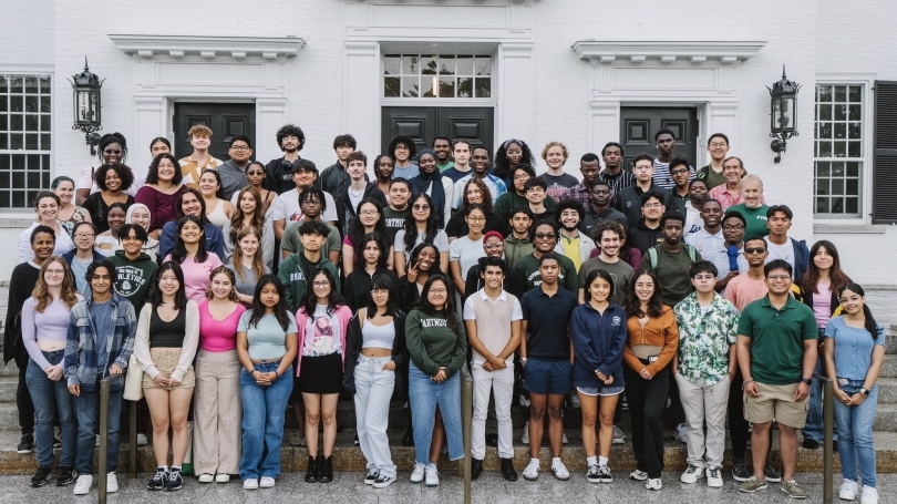 A big group of students line up on a set of stairs in front of the white overlook of Dartmouth Hall. 