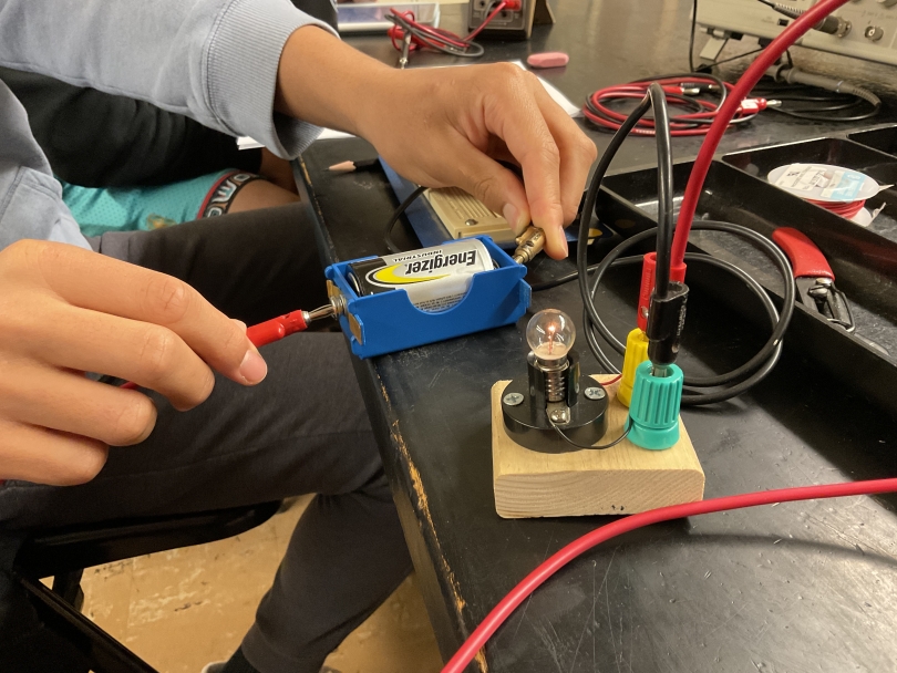 a picture of hands holding a battery and bulb in circuit