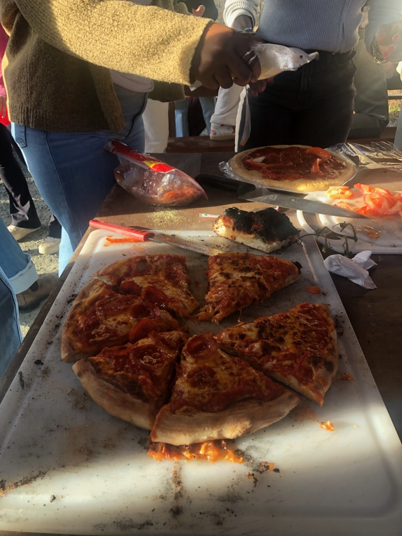 A pepperoni pizza sliced on a white cutting board on a wooden picnic table.