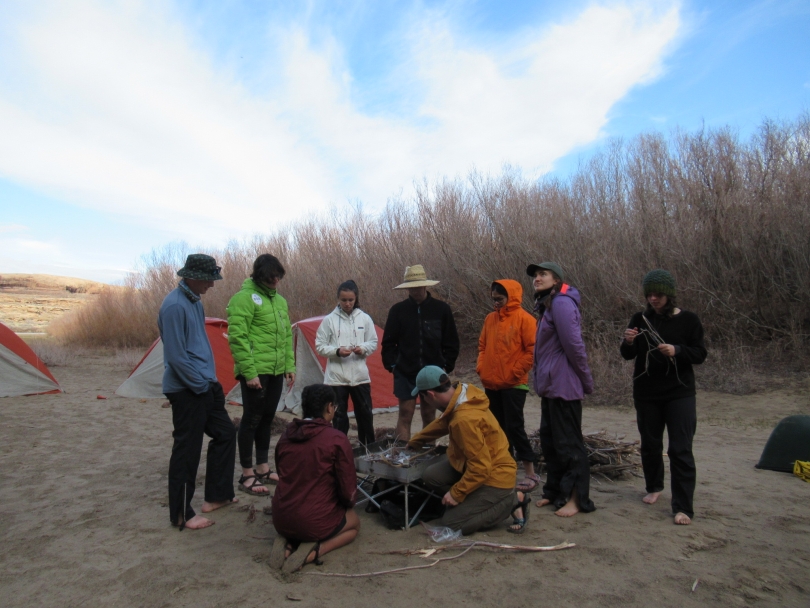 Students huddling around campfire during first rainy day of break trip