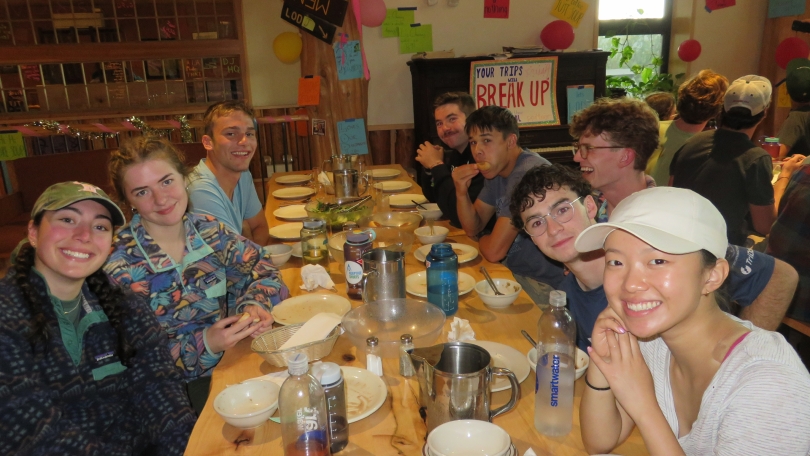 An image of me, Crystal, and my trip group at Moosilauke Ravine Lodge, seated around a long table. The table is plated for dinner and there is a salad in the middle of the table.