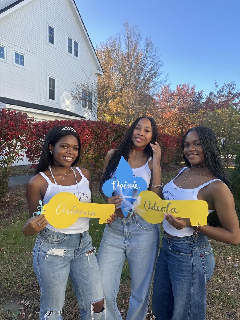 Three girls holding their blue and yellow name tags and white tank tops with blue lettering..