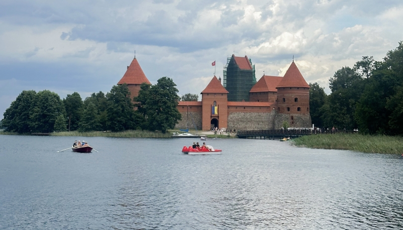 Photo of red-brownish colored Trakei Island Castle in Lithuania with people canoeing in front of it