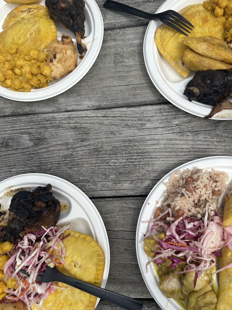 Four plates of Caribbean food are sitting in the center of a picnic table.