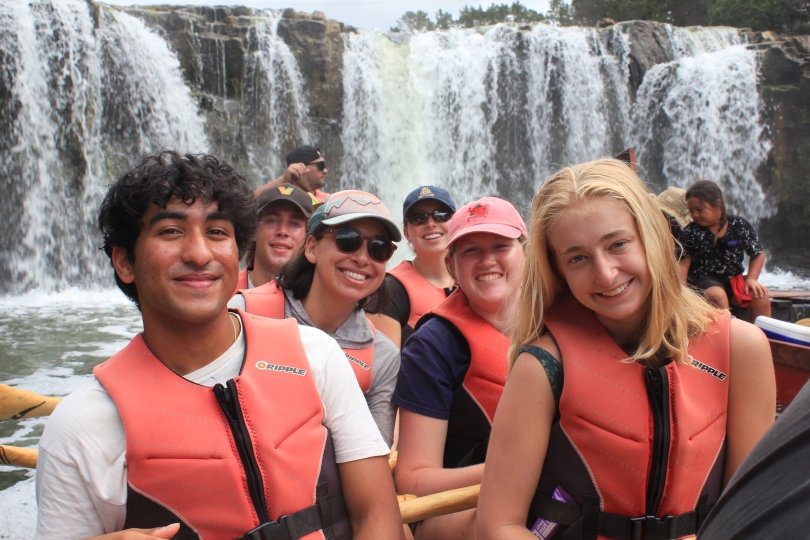 Students smiling in a large canoe in front of a waterfall