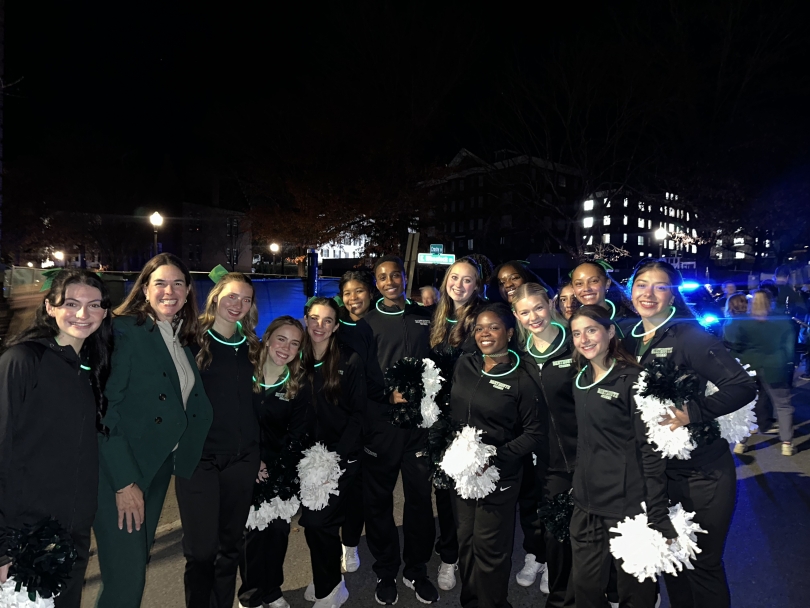 The Dartmouth cheerleading team wearing glow stick necklaces and holding pom-poms, posing with President Beilock.