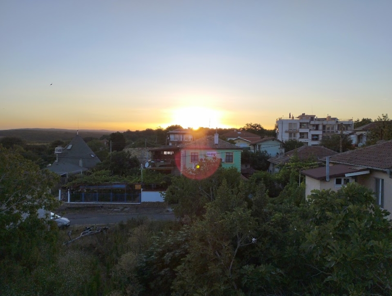 a picture of the sun setting behind a number of traditional Bulgarian houses 