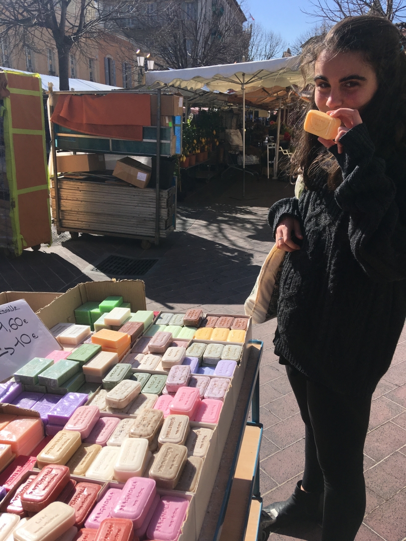 Sarah sniffing soap at laden market table