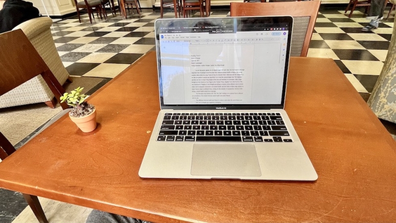 A computer with an open document--an academic assignment--and a succulent plant on a wooden table in Baker Berry library