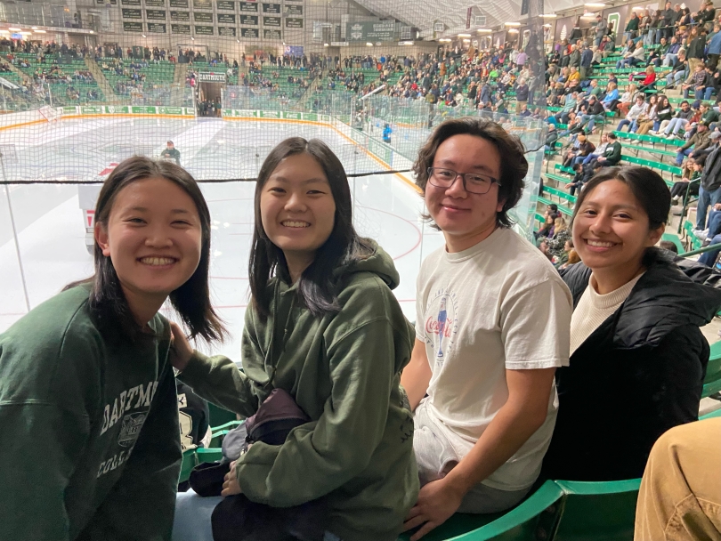 Group of four people sitting down in a hockey arena and wearing green 