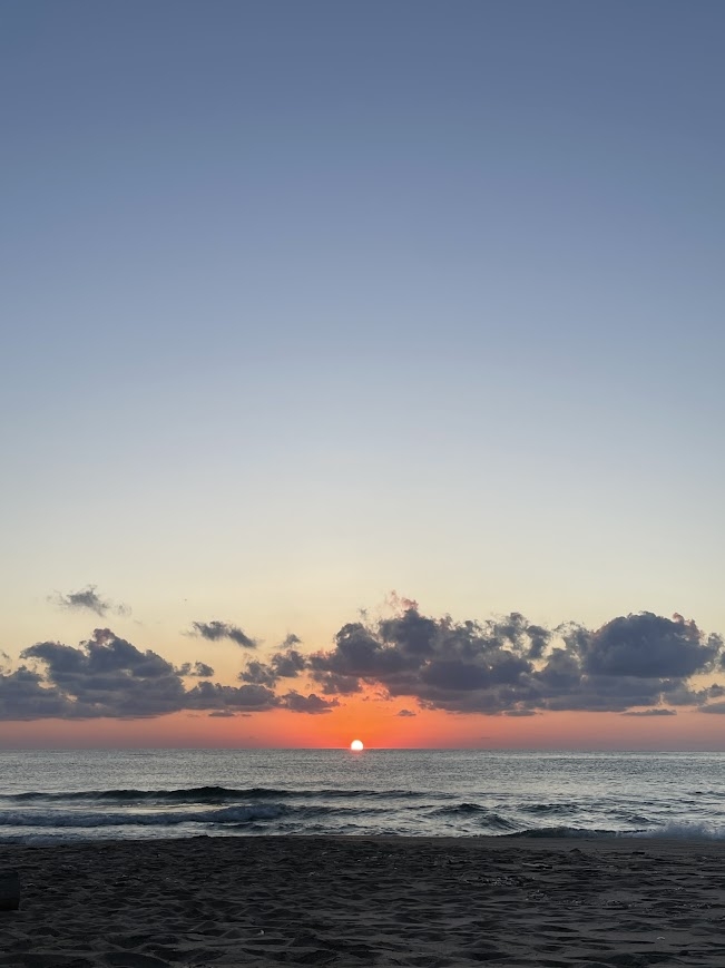 a picture of a sunrise over the sea with feathery clouds near the horizon