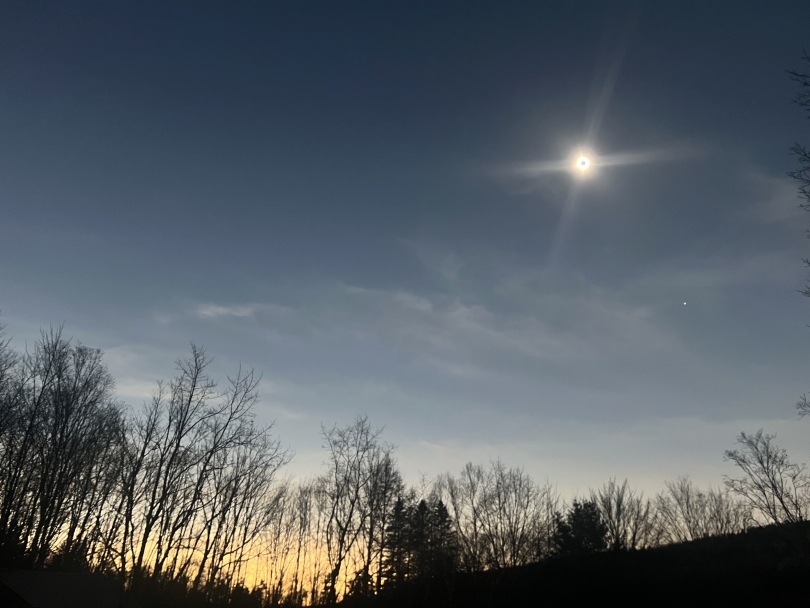 a view of the darkened sky during the solar eclipse, a warm orange in the distance and the glowing red ring in the center of the sky