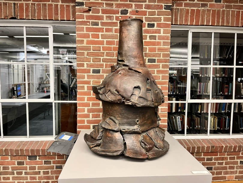 A photo of a large bronze sculpture in front of a brick wall.