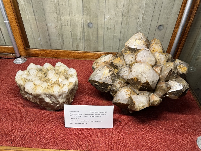 Two huge crystal formations sit on a piece of red fabric in a glass case