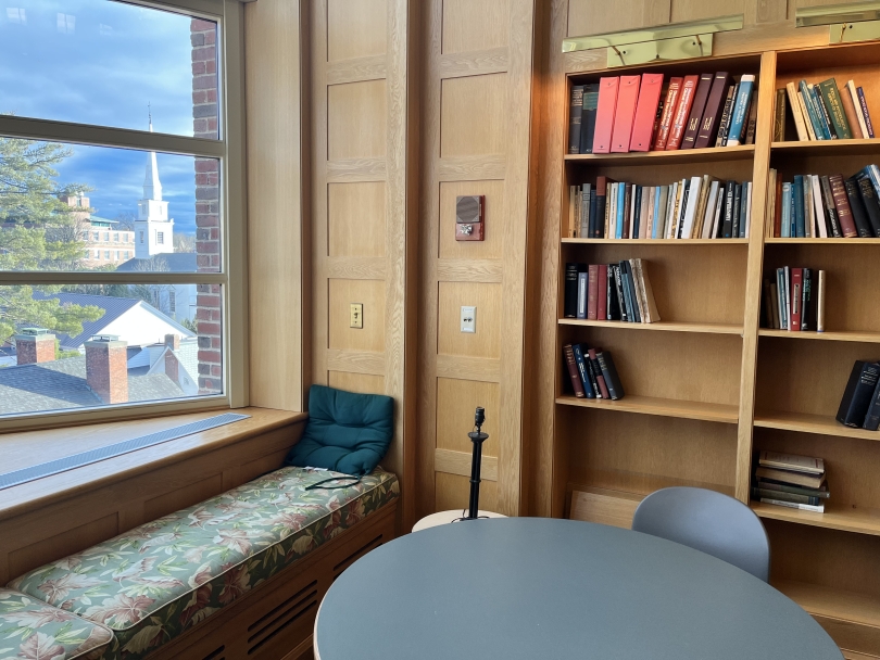 A cozy corner sofa bench next to a window in a library. The cushions are floral patterned and outside the window, you can see a church steeple against a backdrop of brilliant blue.