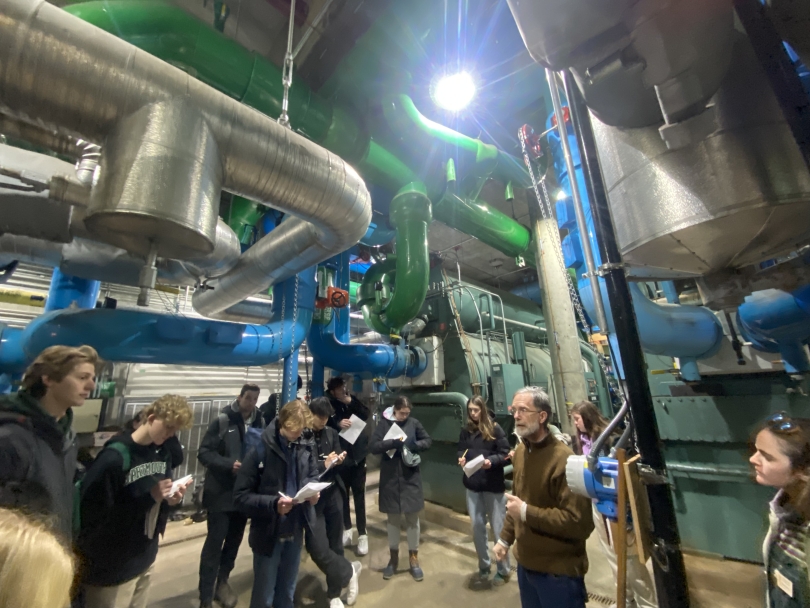 a picture of several students huddled in a basement of Dartmouth's Water chilling plant, tubing all over the room, while a tour guide explains what they're looking at