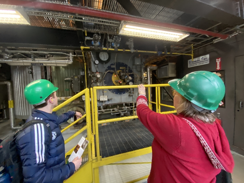 a picture of the tour guide pointing towards one of dartmouth's combustion oil boilers, while a student watches from a safe distance.