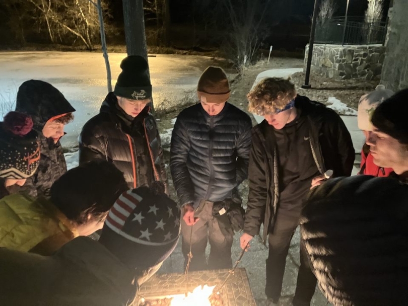 a picture of martin and his friends surrounding a fire pit, roasting marshmellows