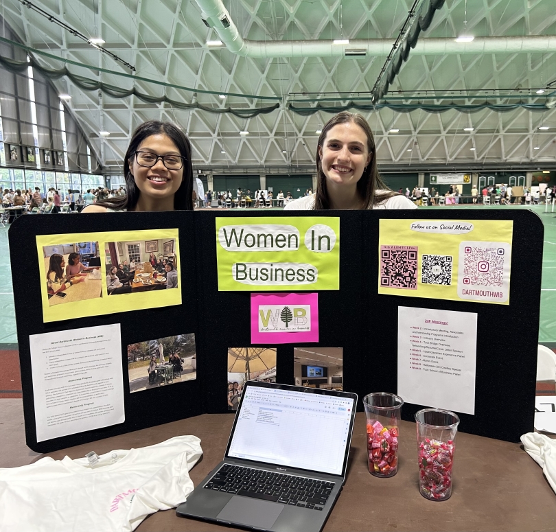 Two girls holding a Dartmouth Women in Business poster at the club fair