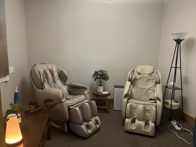 An image of a room with two full body massage chair, and a lamp in the corner.