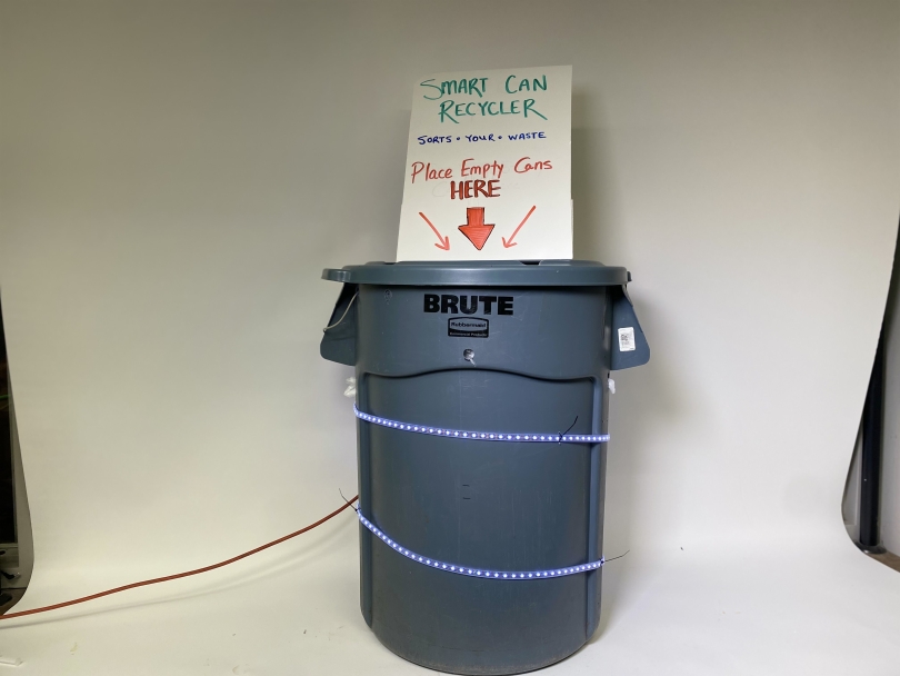a tall trash can wrapped in LEDs with a sign on top, saying "place cans here!"