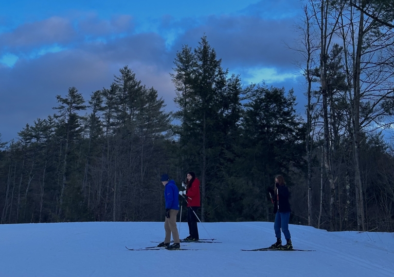 Three individuals using ski gear trudge through the white snow.