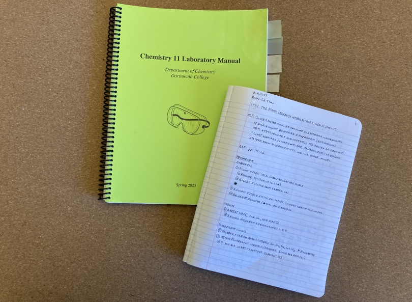 A photo of a lime green chemistry eleven lab notebook and an open composition notebook with laboratory procedures written in black pen