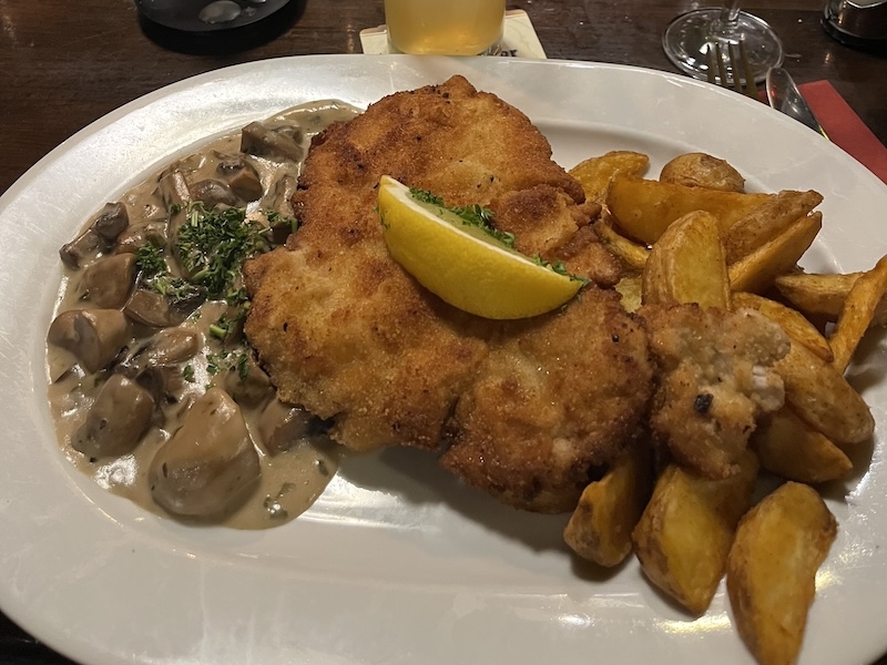 An image of a plate of food with schnitzel, mushrooms and potatoes