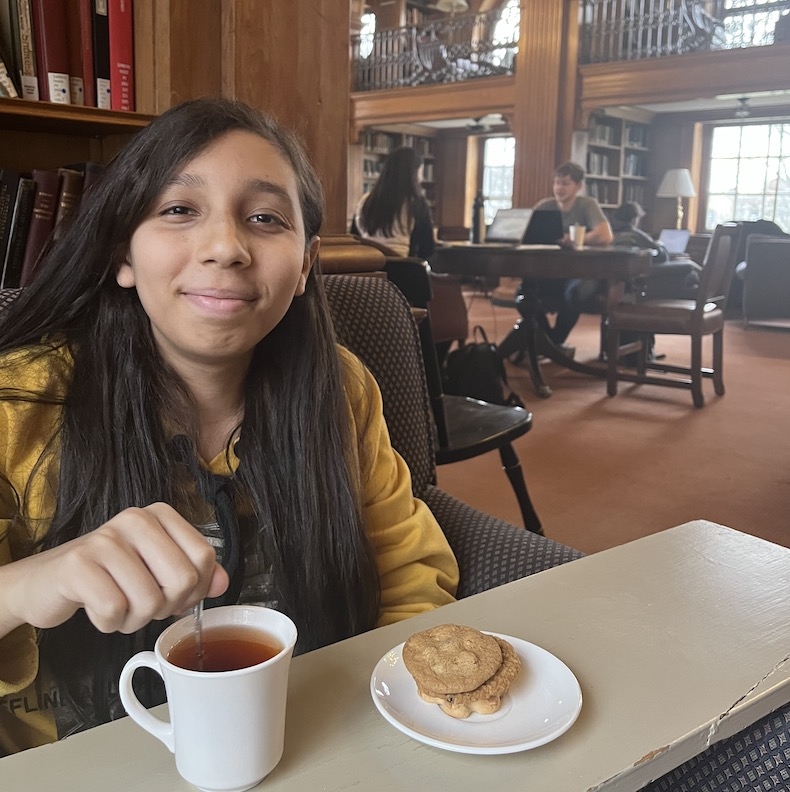 An image of a student sitting Sanborn Library and drinking tea.