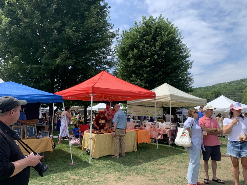 Multi-colored tents and vendor tables with groups of buyers surrounding them