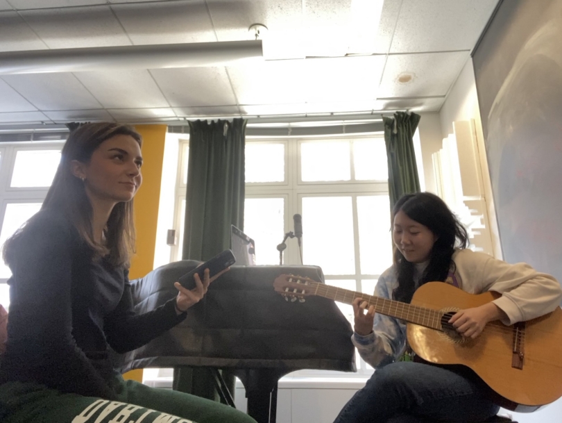 an image of two women in a room, one is playing a guitar and both are about to sing