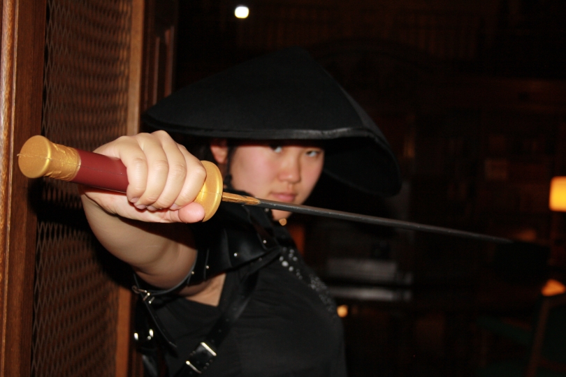 This is a photo I took of one of my friends in the tower room. The focus is on her costume sword with her in the direct background and then the central part of the dark tower room behind her.