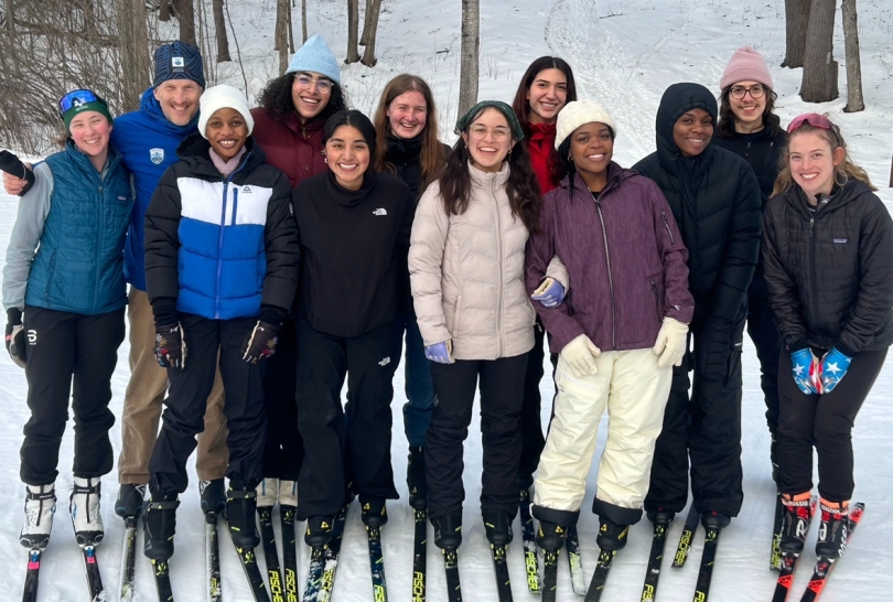 A group of smiling individuals with winter gear and skiing equipment in hand.