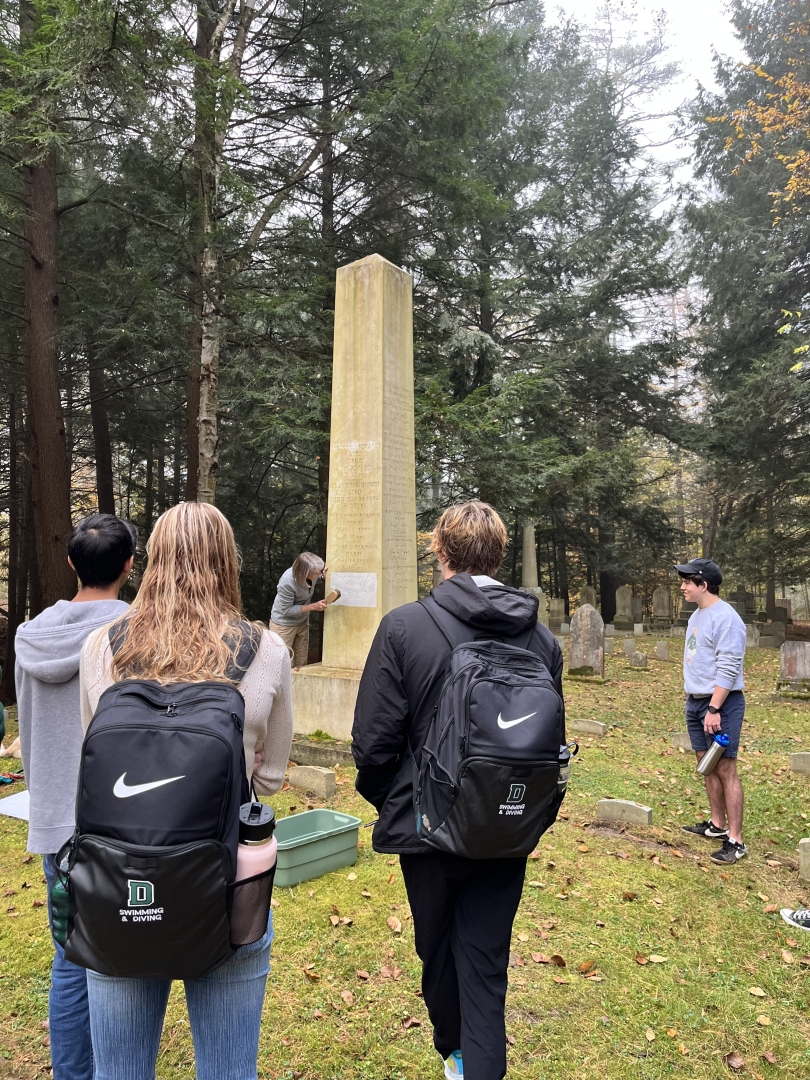 A photo of Professor Lynn making a squeeze of a headstone in the cemetery with several students observing her. 