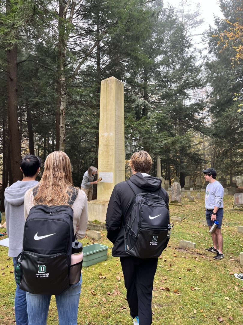 A photo of Professor Lynn making a squeeze of a headstone in the cemetery with several students observing her.