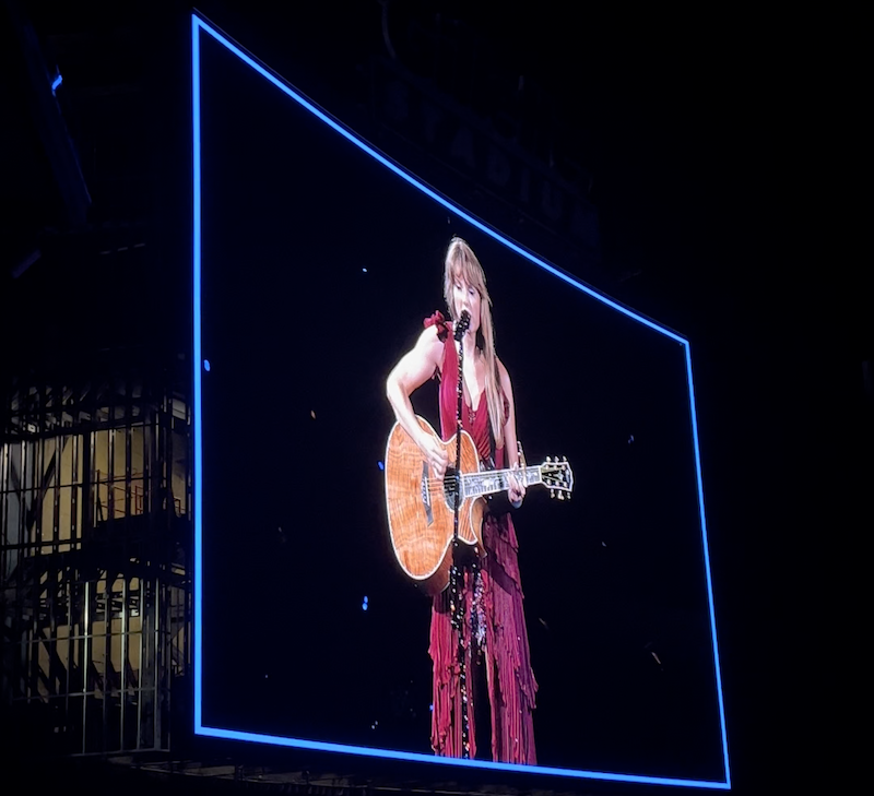 An image of Taylor Swift playing her guitar on stage at a concert