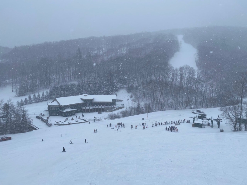 a mid-snowfall picture of the Dartmouth Skiway Lodge from above on the slope, covered in snow.